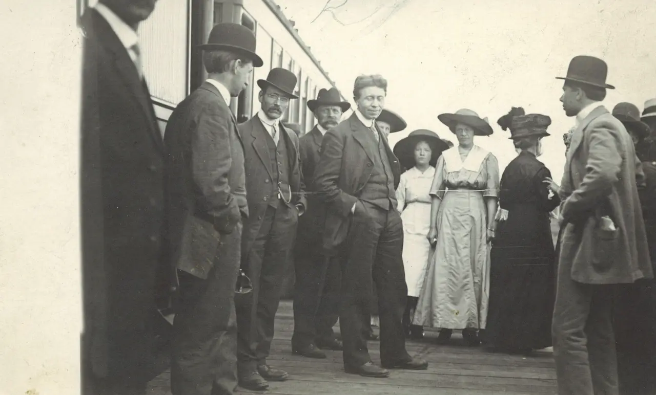 Crowd gathered on the station platform beside a train, about 1910